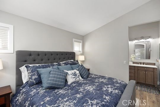 bedroom with vaulted ceiling, connected bathroom, hardwood / wood-style floors, and sink