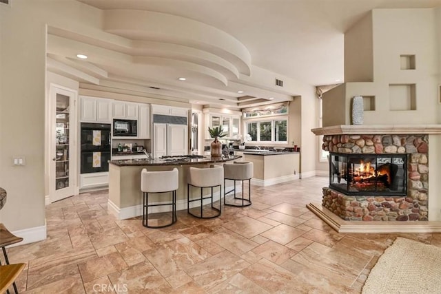 kitchen featuring white cabinetry, a center island, a kitchen breakfast bar, a fireplace, and black appliances