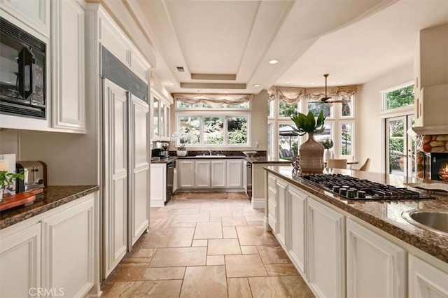 kitchen featuring pendant lighting, white cabinets, black appliances, a stone fireplace, and dark stone countertops