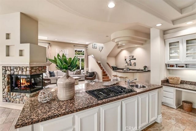 kitchen featuring a fireplace, black gas stovetop, sink, and white cabinets