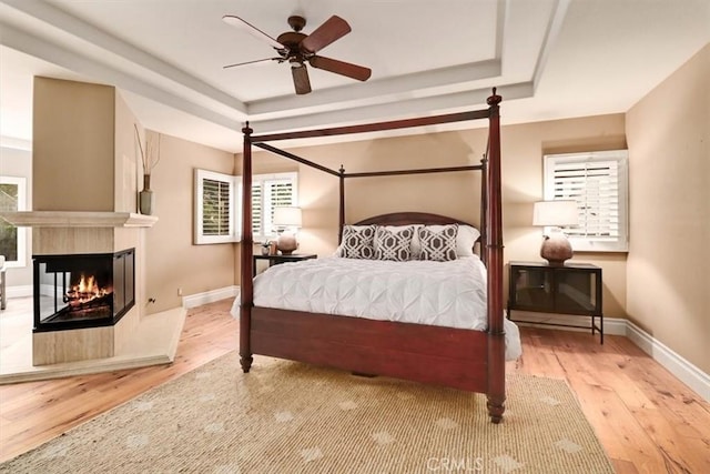 bedroom featuring a multi sided fireplace, multiple windows, ceiling fan, and light hardwood / wood-style floors