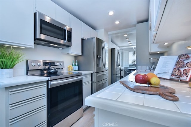 kitchen featuring white cabinets, appliances with stainless steel finishes, and tile counters