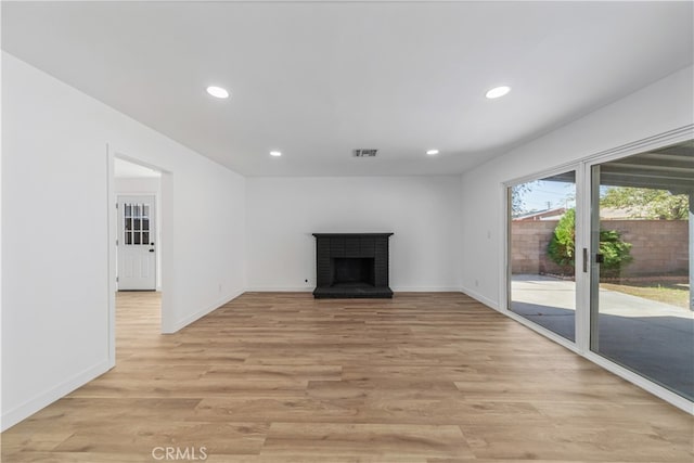 unfurnished living room featuring a brick fireplace and light hardwood / wood-style floors