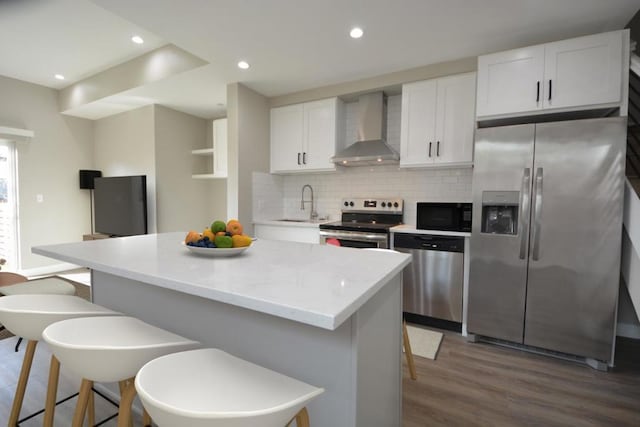 kitchen featuring wall chimney exhaust hood, appliances with stainless steel finishes, a center island, and white cabinets