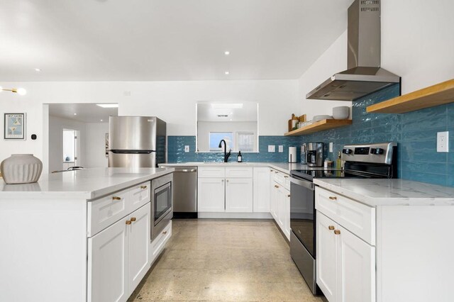 kitchen with appliances with stainless steel finishes, backsplash, sink, wall chimney range hood, and white cabinets