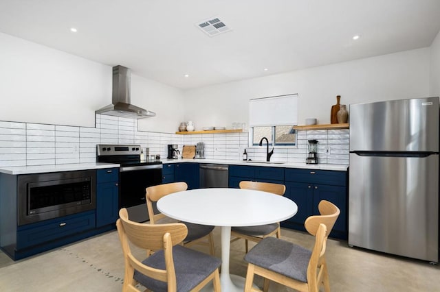 kitchen featuring blue cabinetry, sink, stainless steel appliances, wall chimney range hood, and decorative backsplash