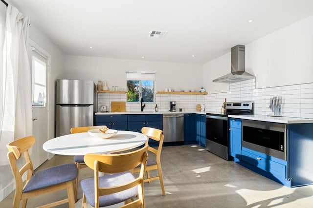 kitchen featuring sink, stainless steel appliances, wall chimney range hood, blue cabinets, and backsplash