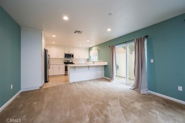 kitchen featuring a breakfast bar, kitchen peninsula, appliances with stainless steel finishes, light colored carpet, and white cabinetry