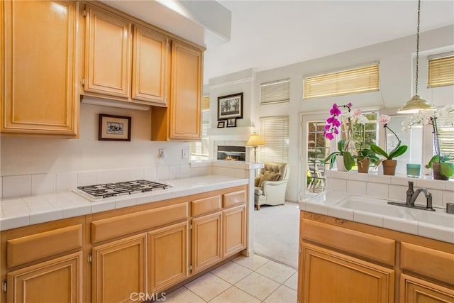 kitchen featuring stainless steel gas cooktop, sink, light tile patterned floors, pendant lighting, and tile countertops