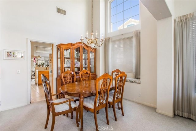 dining area featuring light colored carpet, a towering ceiling, and an inviting chandelier