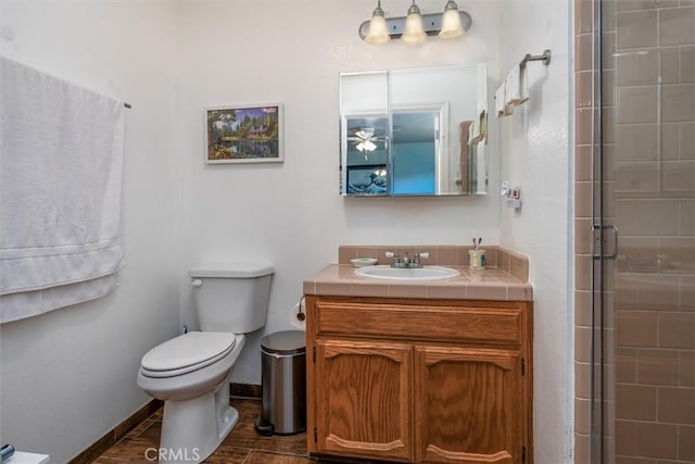 bathroom with toilet, wood finished floors, a tile shower, baseboards, and vanity