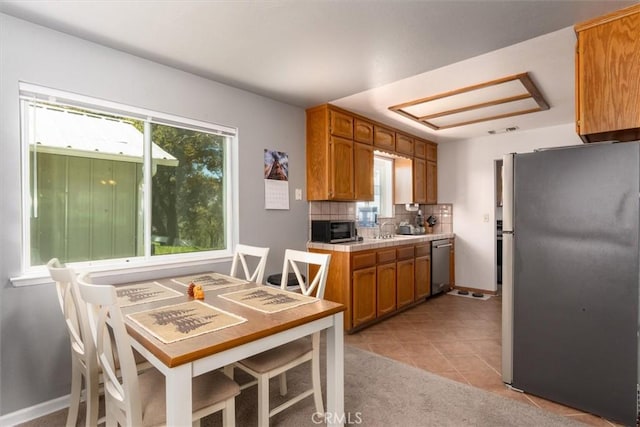 kitchen with brown cabinets, backsplash, appliances with stainless steel finishes, light tile patterned flooring, and baseboards