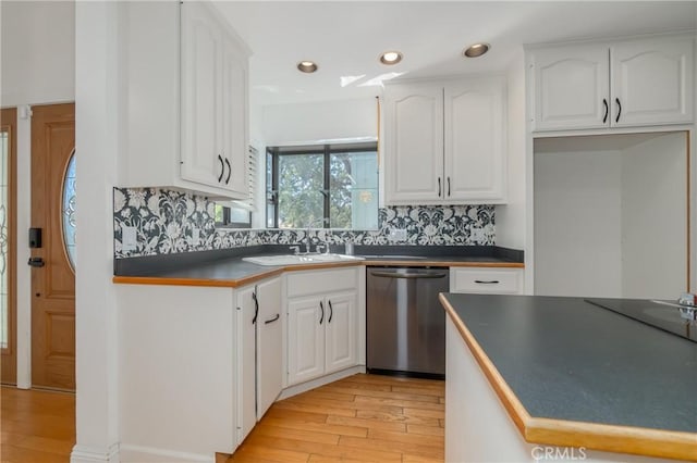 kitchen with dark countertops, light wood-type flooring, stainless steel dishwasher, white cabinetry, and a sink