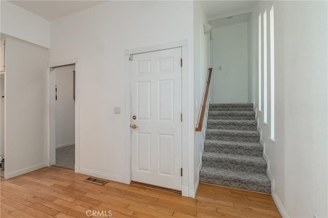 foyer with stairs, light wood-type flooring, visible vents, and baseboards