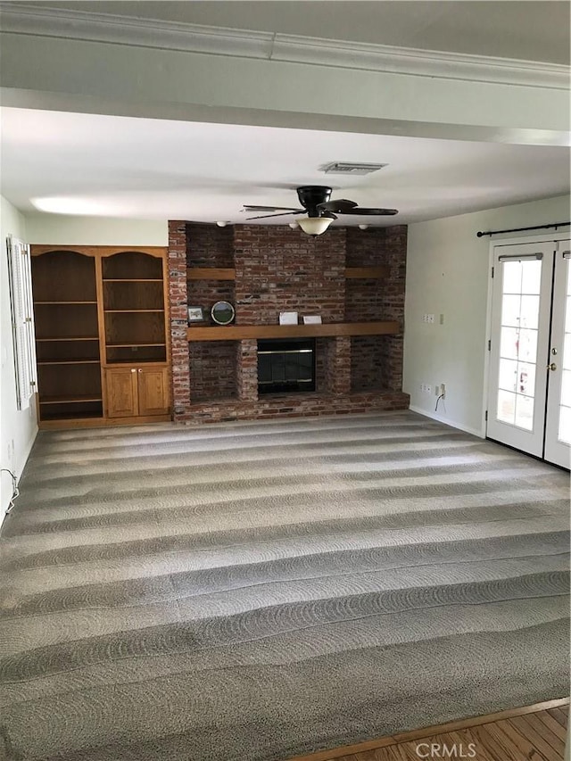 unfurnished living room with carpet, french doors, a brick fireplace, ornamental molding, and ceiling fan