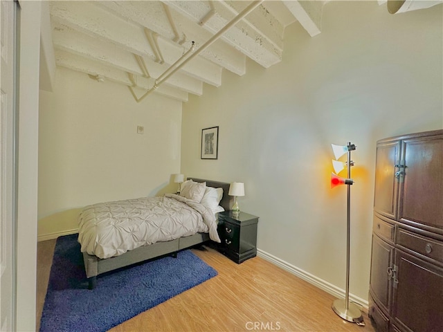 bedroom with light hardwood / wood-style floors and beam ceiling