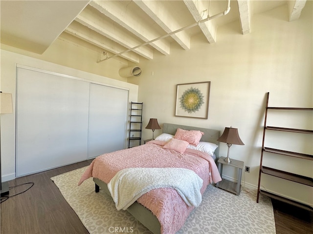 bedroom featuring wood-type flooring, beam ceiling, and a closet