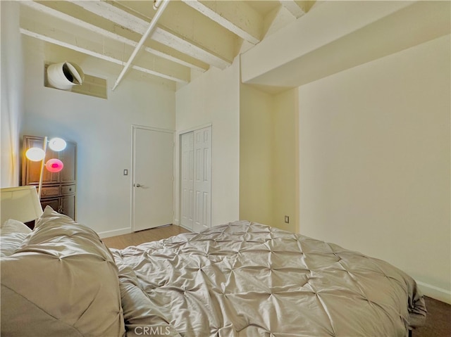 bedroom with wood-type flooring, a closet, and beamed ceiling