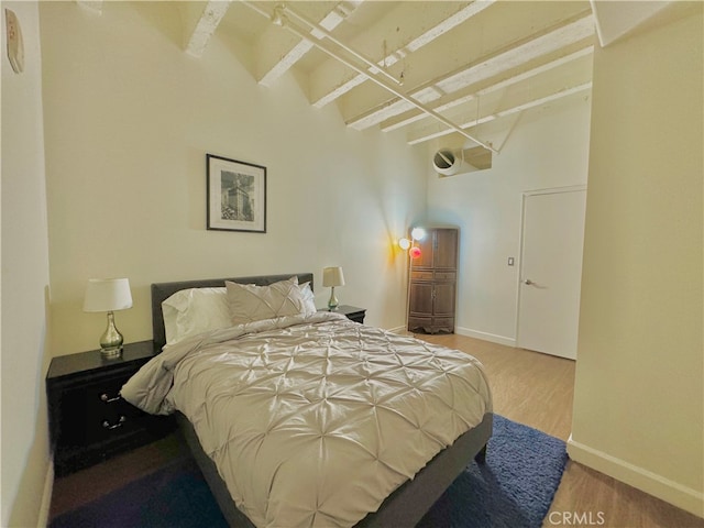 bedroom with light hardwood / wood-style floors and beam ceiling