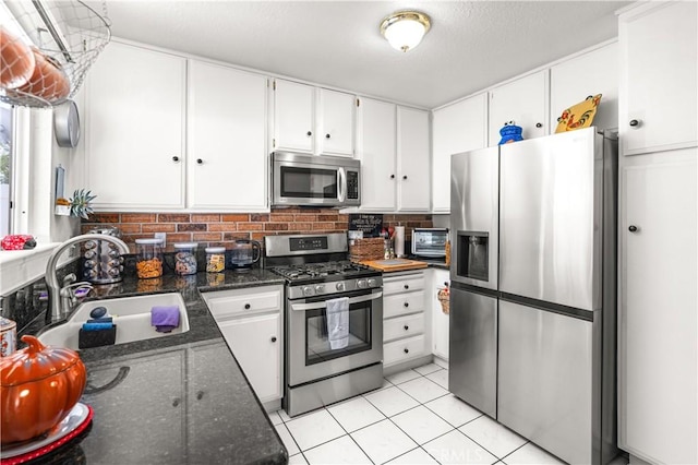 kitchen featuring decorative backsplash, dark stone countertops, light tile patterned floors, appliances with stainless steel finishes, and white cabinetry