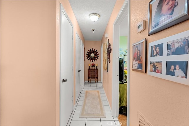 corridor with a textured ceiling and light tile patterned flooring