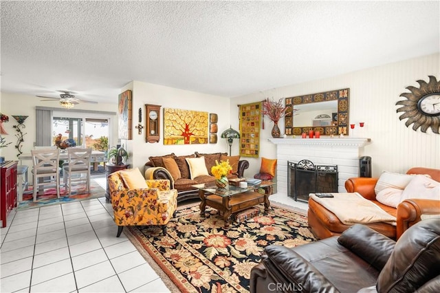 living room with ceiling fan, light tile patterned flooring, a textured ceiling, and a brick fireplace