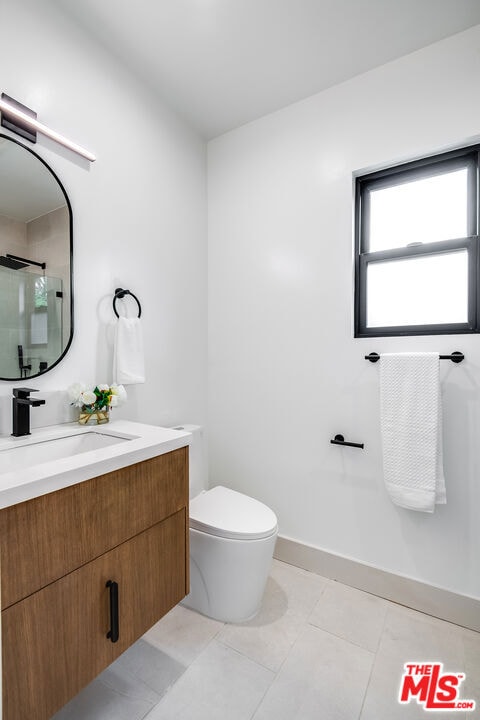 bathroom with toilet, tile patterned floors, vanity, and tiled shower