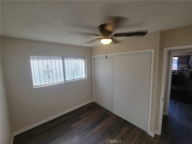 unfurnished bedroom with multiple windows, ceiling fan, dark wood-type flooring, and a closet