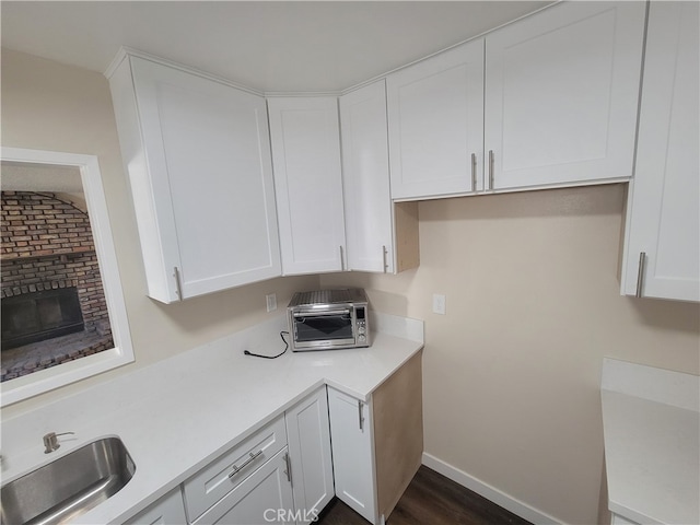 kitchen featuring dark hardwood / wood-style floors, sink, white cabinets, vaulted ceiling, and a fireplace