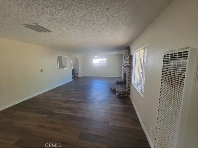 unfurnished living room with a brick fireplace, a textured ceiling, and dark hardwood / wood-style floors