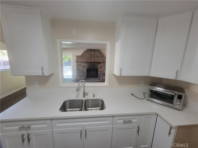 kitchen featuring white cabinets, wood-type flooring, a fireplace, and sink