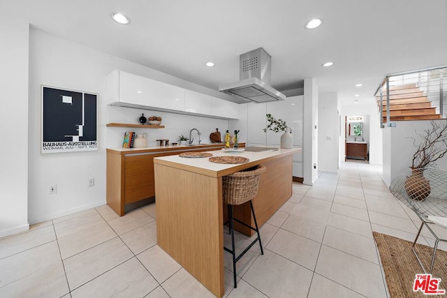 kitchen with a center island, a kitchen bar, sink, white cabinetry, and island range hood