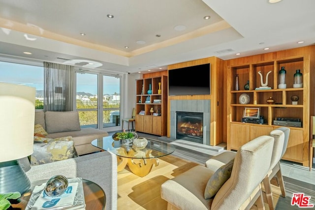 living room featuring built in shelves, a tray ceiling, and light hardwood / wood-style flooring