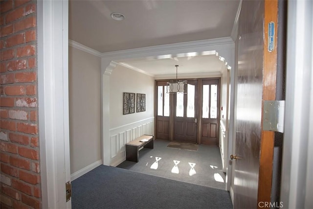 carpeted foyer with ornamental molding and a notable chandelier