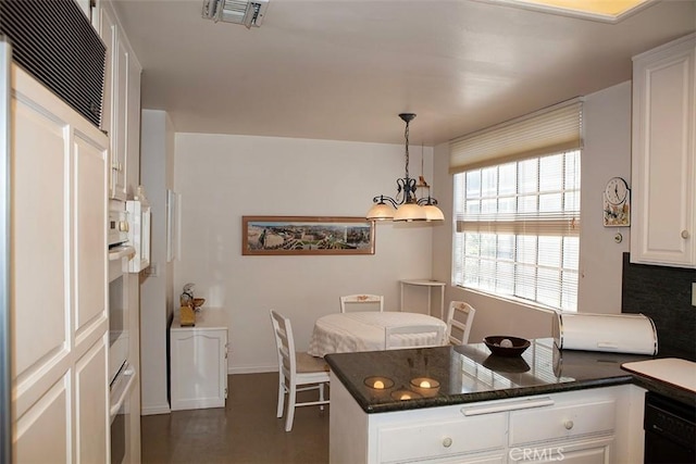 kitchen featuring pendant lighting, dishwasher, dark stone counters, a notable chandelier, and white cabinetry