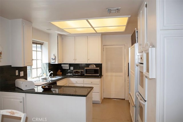 kitchen featuring wall oven, white cabinetry, kitchen peninsula, and sink