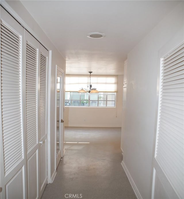 hallway with an inviting chandelier, carpet flooring, and baseboards