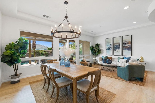 dining space featuring a tray ceiling, a chandelier, and light wood-type flooring