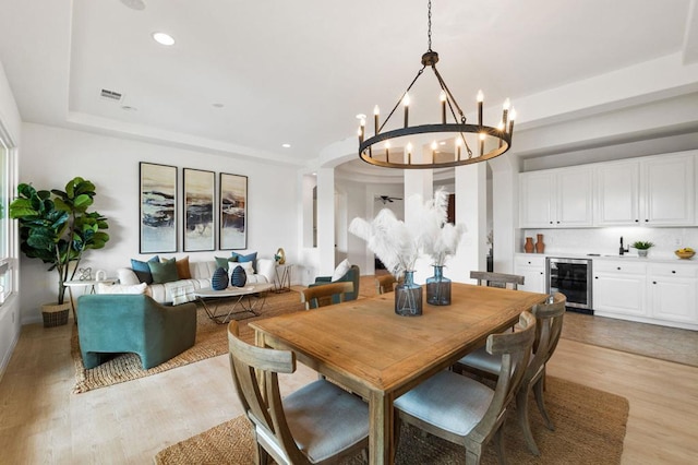 dining space featuring a raised ceiling, wine cooler, an inviting chandelier, and light hardwood / wood-style flooring