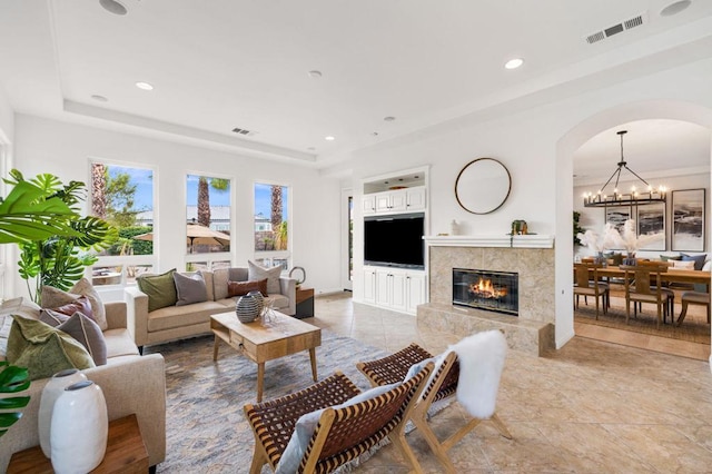 living room featuring a premium fireplace, a tray ceiling, and a notable chandelier