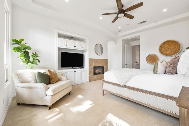 carpeted bedroom featuring a tray ceiling and a tile fireplace