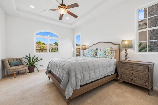 bedroom featuring ceiling fan, a raised ceiling, and light carpet