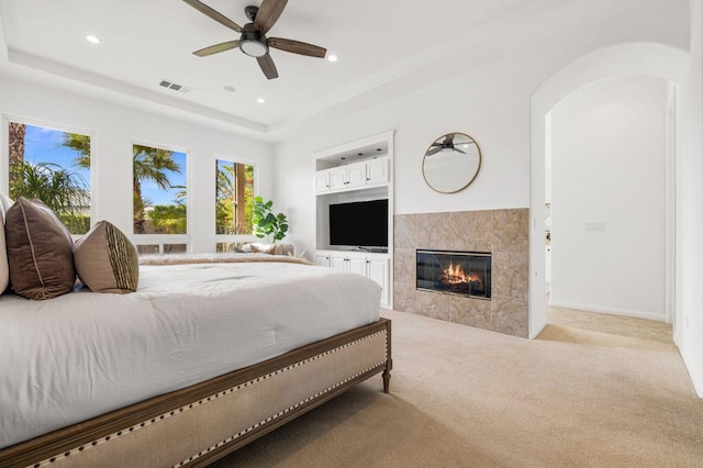 carpeted bedroom with a tray ceiling, a fireplace, and ceiling fan