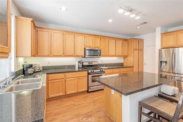 kitchen featuring appliances with stainless steel finishes, light hardwood / wood-style floors, a breakfast bar, a kitchen island, and sink