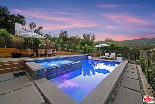 pool at dusk with a mountain view, an in ground hot tub, and a patio area