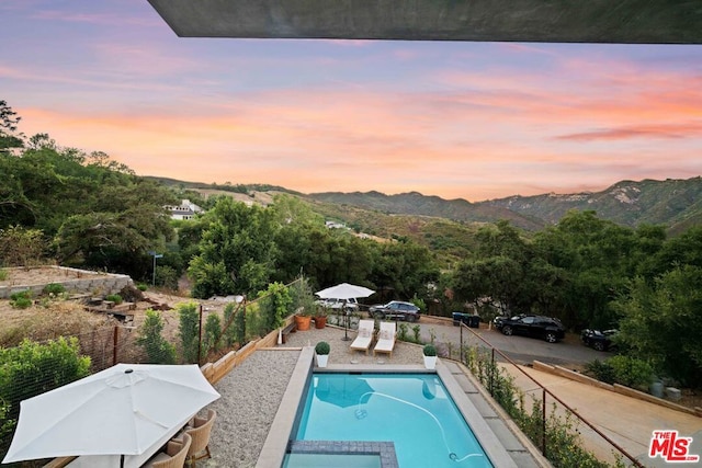 pool at dusk featuring a mountain view and a patio area