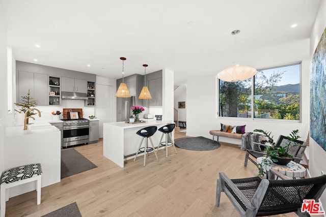 kitchen with kitchen peninsula, decorative light fixtures, light hardwood / wood-style flooring, a breakfast bar area, and gas stove