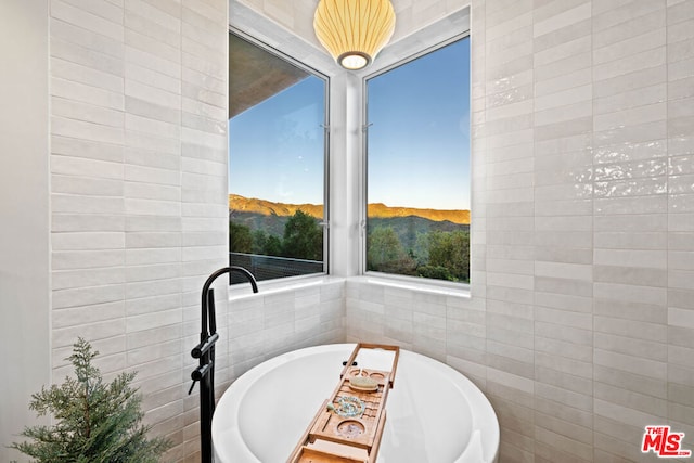 bathroom with a bath, a healthy amount of sunlight, tile walls, and a mountain view