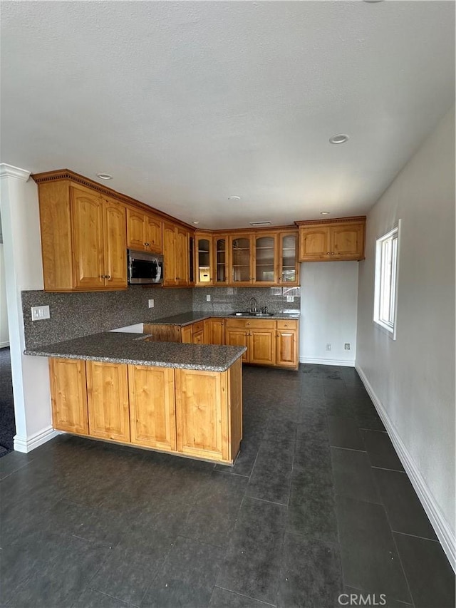 kitchen featuring backsplash, kitchen peninsula, dark stone countertops, and dark tile patterned floors