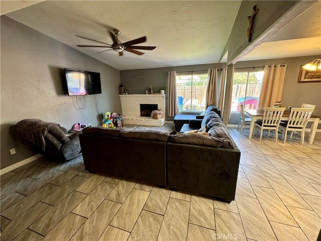 living room featuring a brick fireplace, ceiling fan, a textured ceiling, and vaulted ceiling